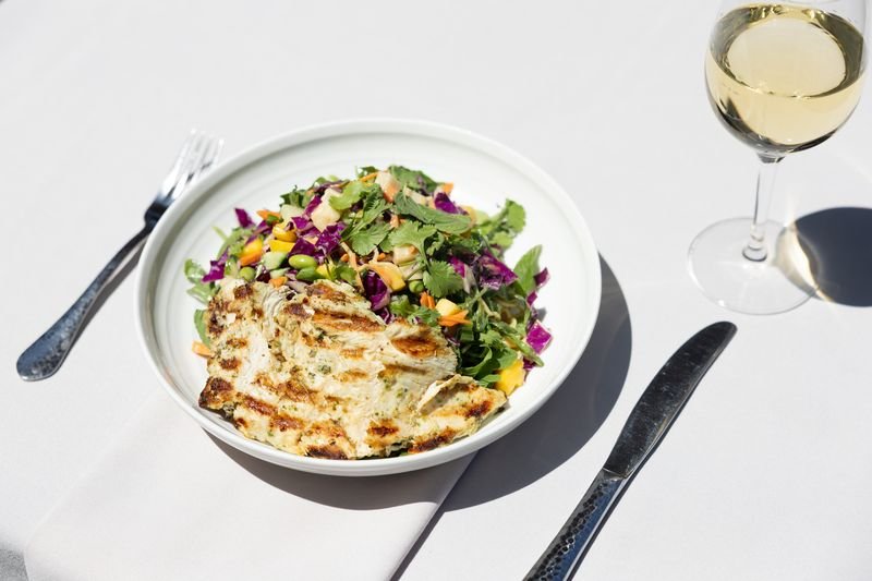 Photo of the Mango Noodle Salad with Chicken at The Restaurant, served with a glass of white wine.
