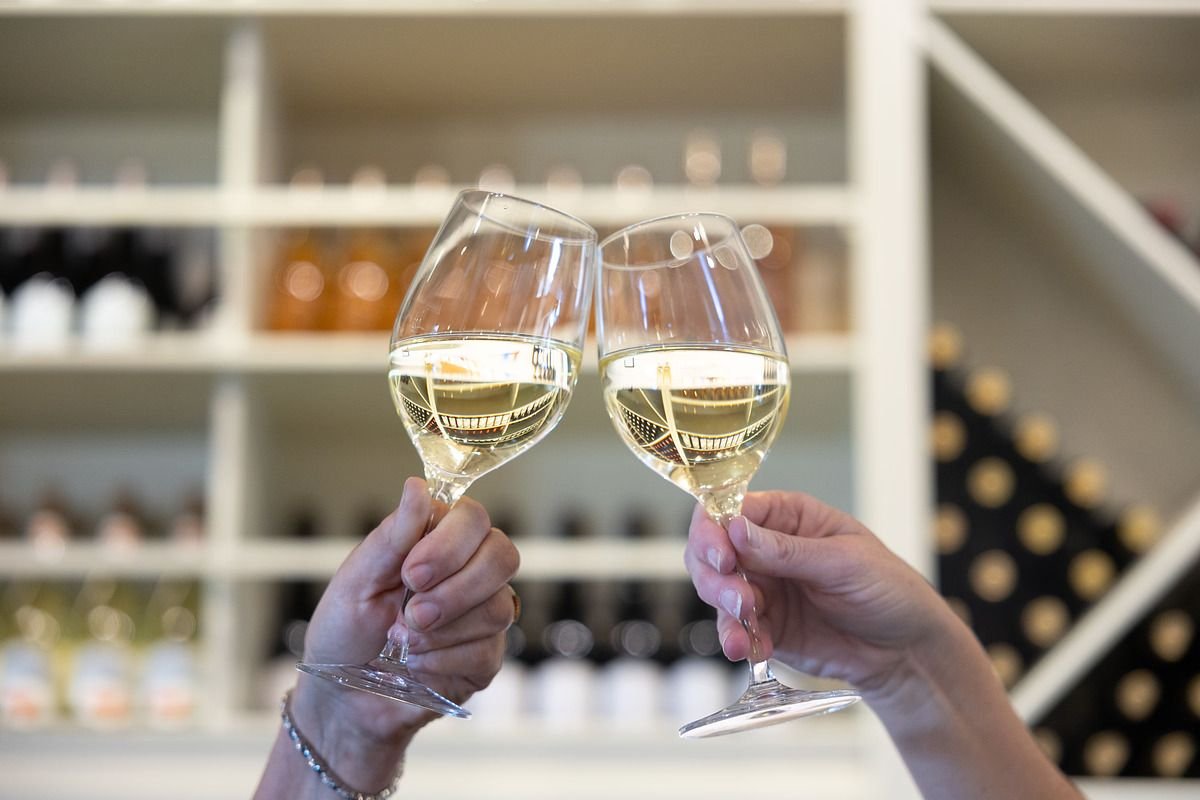 Photo of two hands cheering glasses of white wine.