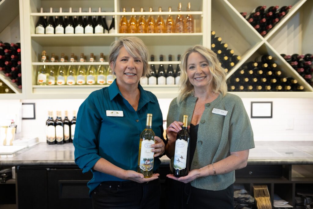 2 tasting room servers holding glasses of wine.