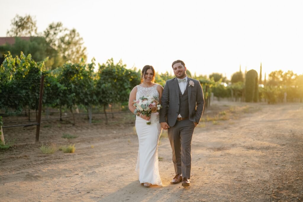 A photo of the bride and groom in front of the vineyard with the sunshine in the background.