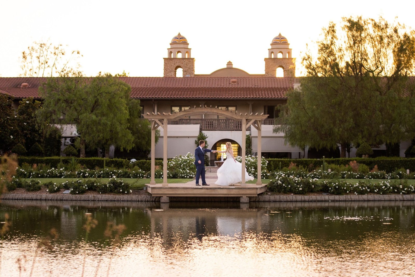 Wedding photo of a couple underneath an arch at Ponte Vineyard Inn in front of a pond.